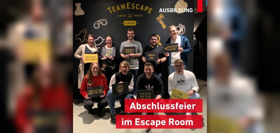 Sechs ehemalige Auszubildende und ihre vier Ausbilder stehen beisammen und schauen in die Kamera. Dabei halten alle humorvolle Schilder in die Höhe, die das Thema Teambuilding umfassen.