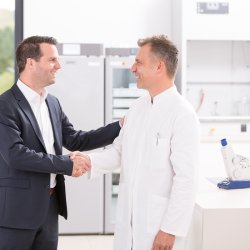 Ein Mann mit einem schwarzen Anzug schüttelt einem Apotheker die Hand