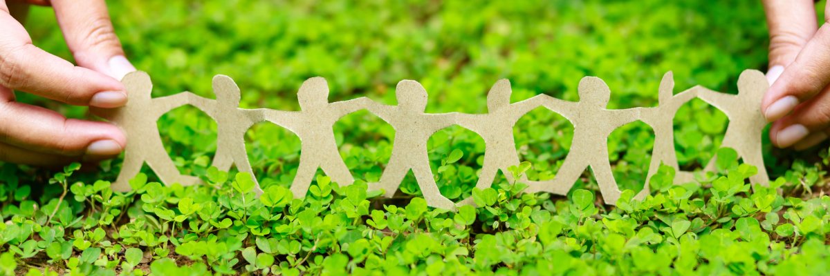 Eine grüne Wiese ist zu sehen auf welcher Pappmännchen in einer Girlande stehen.