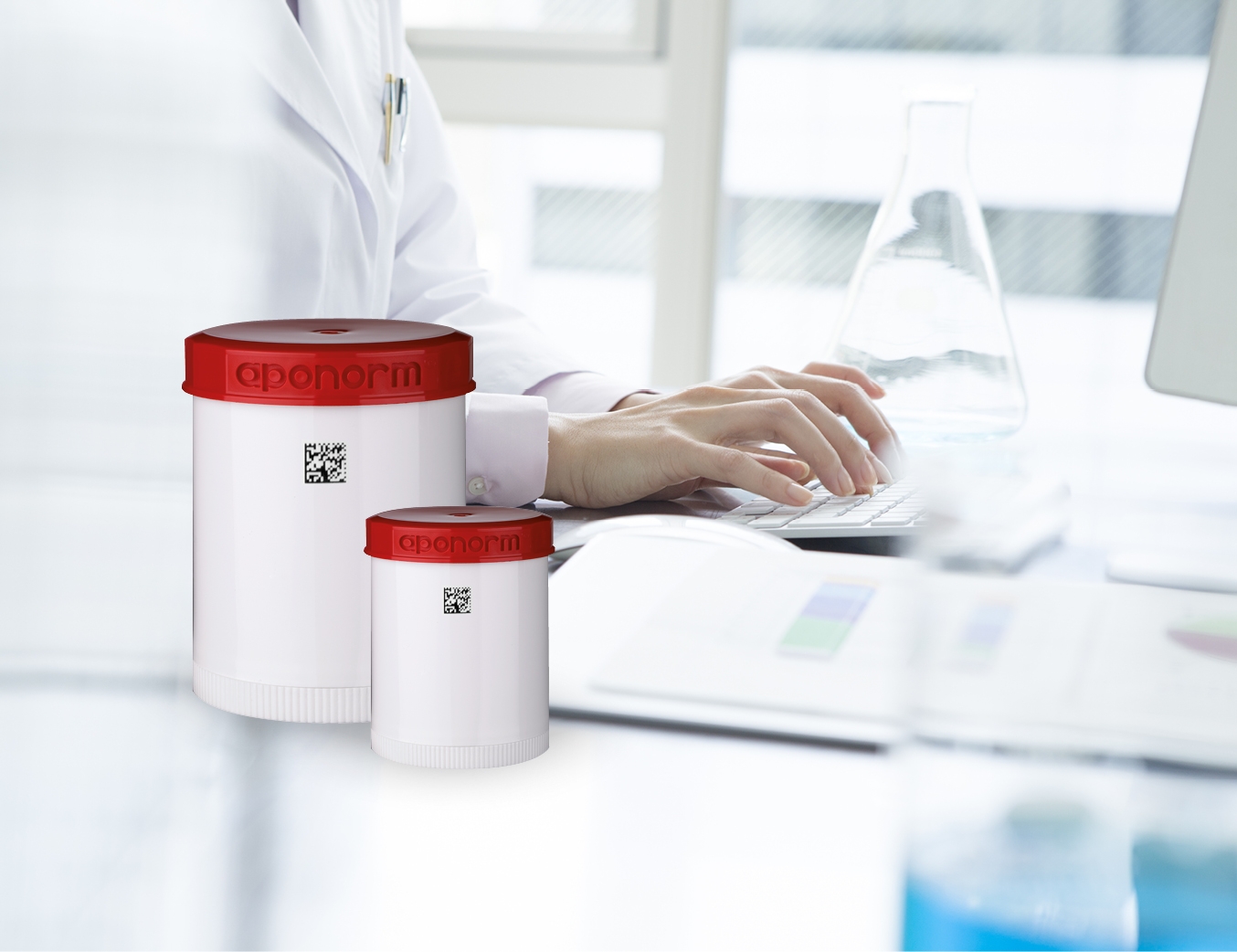 Person sitzt vor dem Computer und tippt auf der Tastatur. Im Vordergrund sind zwei Aponorm Kruken zu sehen.