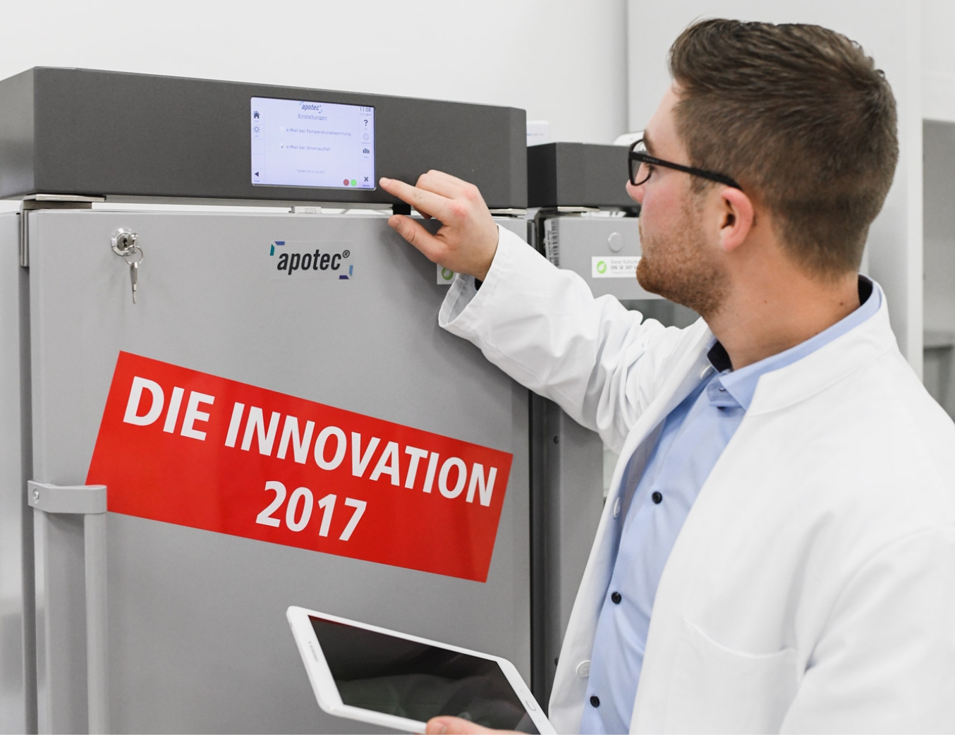 apotec Kühlschrank. Ein Apotheker schaut sich die Kühlregelung eines apotec Kühlschrankes an. Auf dem Kühlschrank steht die Innovation 2017.
