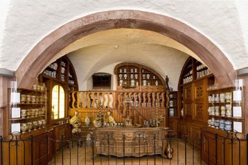 Das deutsche Apothekenmuseum in Heidelberg ist zu sehen. Apothekenbedarf in holzfarbenden Regalen sind dort platziert.